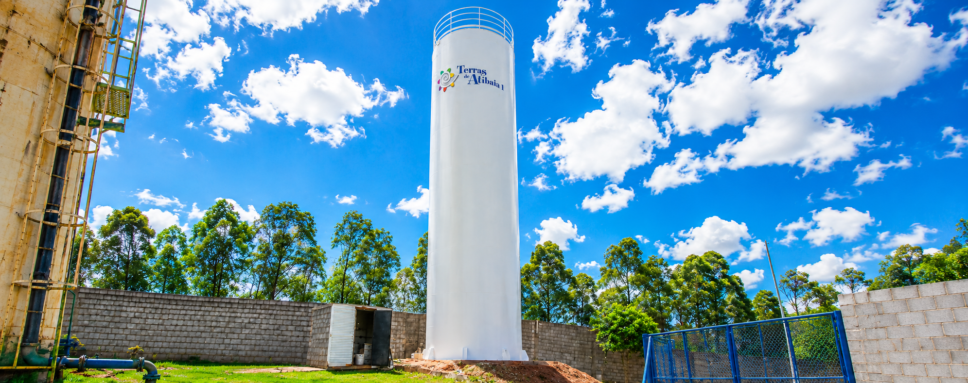 Caixa d'água tipo taça em área rural com céu azul e árvores